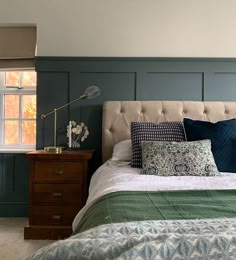 a bed with blue and green pillows on top of it next to a window in a bedroom