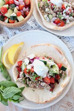 there are two tacos on the table with vegetables and lemon wedges next to it