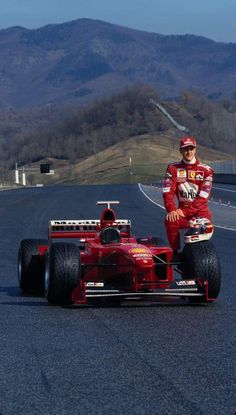 a man standing next to a racing car on a race track with mountains in the background