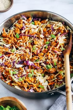 a pan filled with coleslaw and meat on top of a table next to two wooden spoons