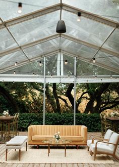 a couch and some chairs under a white tent with trees in the backgroud