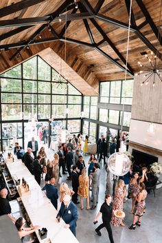 a large group of people standing in a room with lots of windows and tables full of food