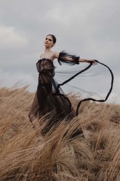 a woman in a black dress standing on top of a grass covered hill