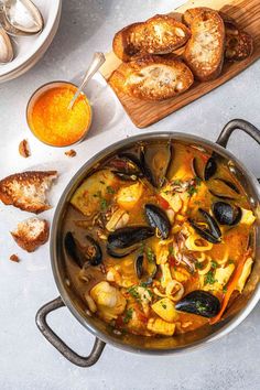 a pan filled with mussels and sauce next to bread