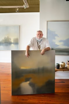 a man standing behind a large painting on top of a hard wood floored floor