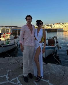 a man and woman standing next to each other in front of boats on the water