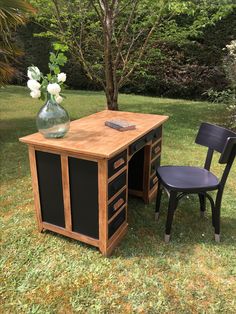 a desk with two chairs and a vase on it sitting in the grass next to a tree