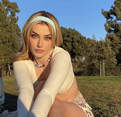 a woman sitting on top of a grass covered field with trees in the back ground