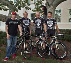 three men are posing with their bikes in front of a tree and some people standing next to them