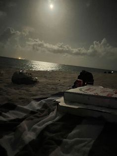 the sun is setting over the ocean and some people are laying in the sand on the beach