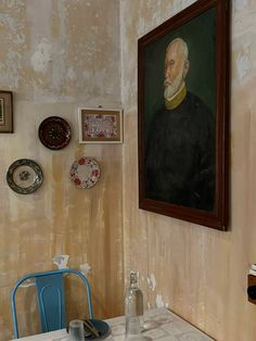 a painting hangs on the wall above a dining room table with blue chairs and plates