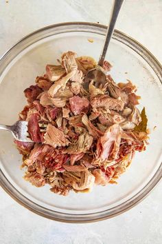 a glass bowl filled with meat and vegetables on top of a table next to a spoon