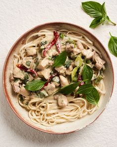 a white bowl filled with pasta covered in sauce and vegetables on top of a table