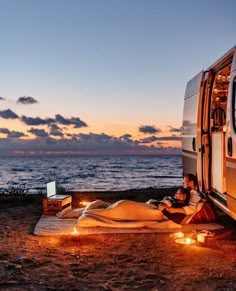 two people sitting on the ground next to an rv with lights in front of them