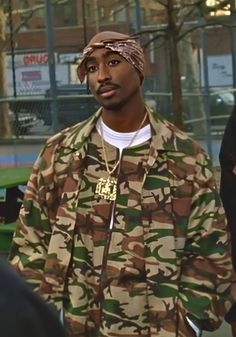 a man in camouflage jacket and bandana standing next to other people on the street