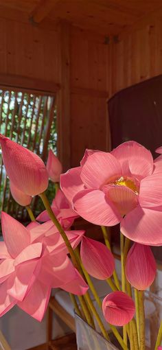 pink flowers are in a clear vase on a table next to a wooden window sill