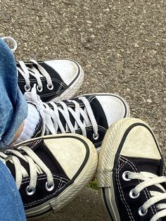 a person wearing black and white converse shoes with their feet up on the ground next to each other