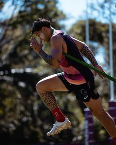 a man with tattoos on his arms and legs is jumping in the air while holding a green pole