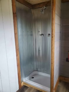 a bathroom with a walk in shower next to a wall mounted faucet and wood flooring