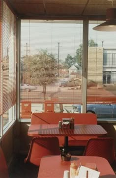 an empty restaurant with red tables and chairs in front of large windows that look out onto the parking lot