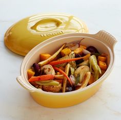 a yellow casserole dish filled with assorted veggies next to a yellow lid