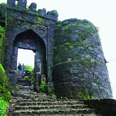 an old stone castle with stairs leading up to the entrance and two people standing at the top