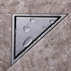 a triangle shaped shower drain with water droplets on it