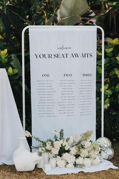 a white sign sitting on top of a grass covered field next to flowers and vases