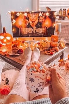 a person holding a cup with candy in front of a halloween scene on the tv