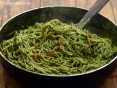 a pan filled with green pasta on top of a wooden table