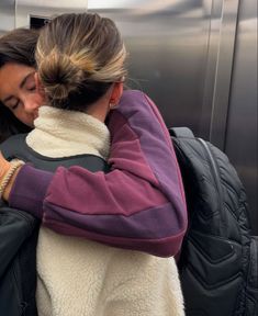 two women hugging each other while standing in front of a metal door with their arms around each other