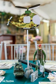 a table topped with toy soldiers next to a green table cloth covered tablecloth and white chairs