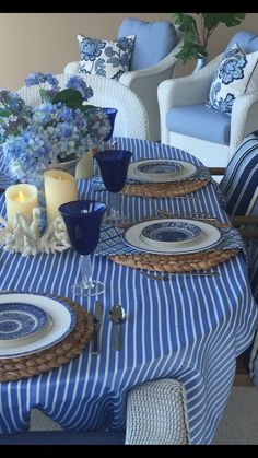 a blue and white table setting with candles, plates and flowers on the dining room table