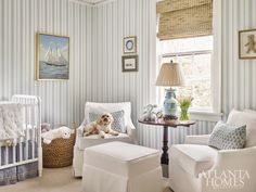 a baby's room with blue and white striped wallpaper, two chairs, a crib and a dog sitting on the floor