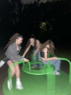 three girls are playing on a green trampoline in the park at night time