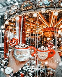 two people holding mugs with candy in front of a merry - go - round carousel