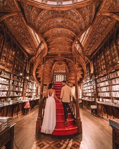 a man and woman standing on top of a red staircase in front of bookshelves