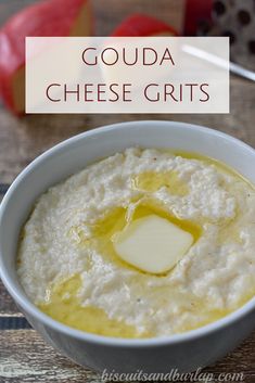 a white bowl filled with cheese grits on top of a wooden table next to an apple