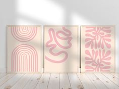 three pink and white art pieces on a wooden floor in front of a white wall