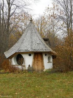 a small white and brown house in the middle of a field with lots of trees