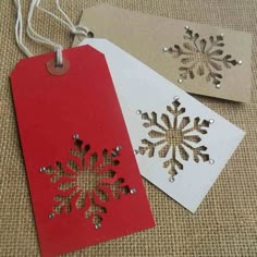 two tags with snowflakes on them are sitting next to each other, one is red and the other is white