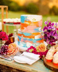 a colorful cake sitting on top of a wooden table next to other desserts and flowers