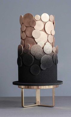 a black and gold wedding cake with circles on the top is sitting on a metal stand