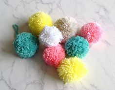 six pom - poms on a marble countertop, all in different colors