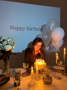 a woman blowing out candles on a birthday cake with balloons and flowers in the background