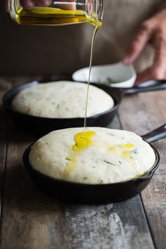 a person pouring olive oil on top of two black pans filled with cheese grits