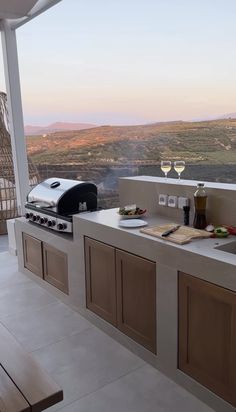 an outdoor kitchen with a grill, sink and wine glass on the counter top overlooking a valley