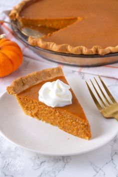 a slice of pumpkin pie on a white plate with a gold fork next to it