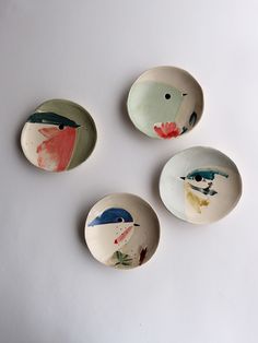 three plates with birds painted on them sitting next to each other in front of a white wall