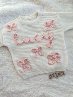 a white sweater with pink bows and the word love written in cursive writing